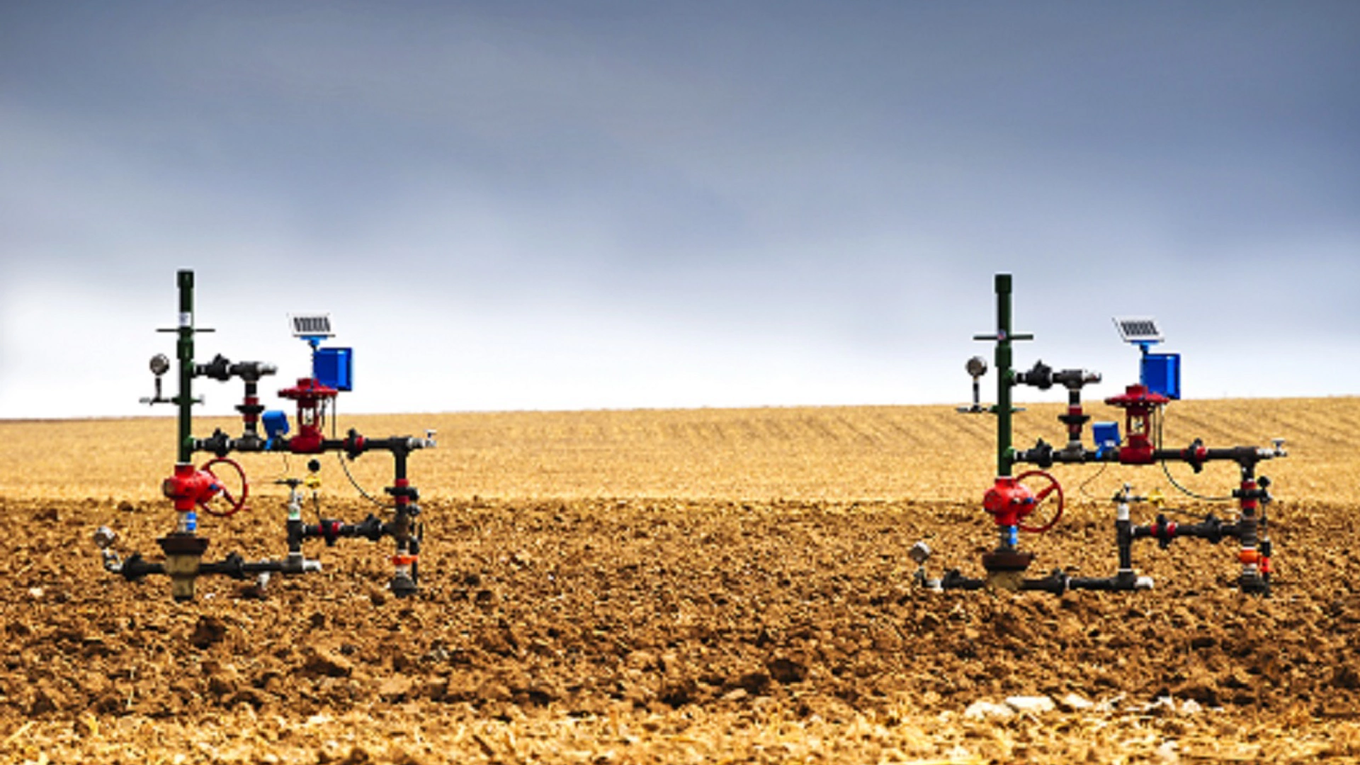 Natural gas wellheads in a plowed cornfield.