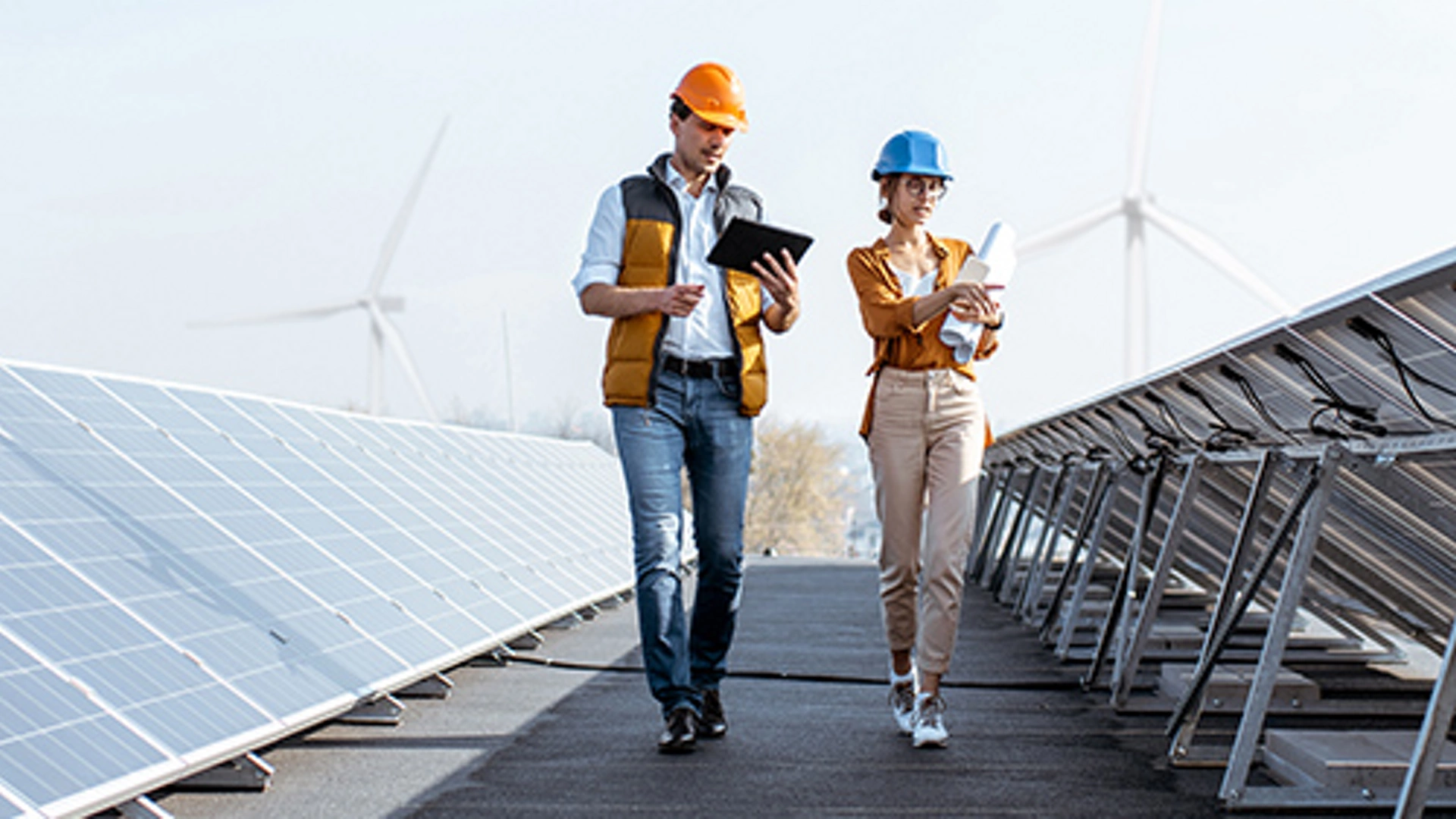 View on the rooftop solar power plant with two engineers walking and examining photovoltaic panels. Concept of alternative energy and its service